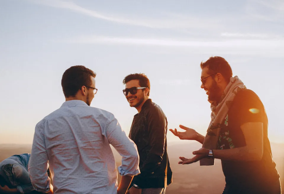 Três amigos conversando e rindo ao ar livre, ao pôr do sol