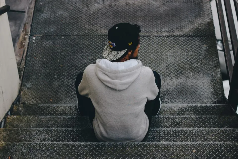 Jovem de moletom sentado sozinho em uma escada, de costas