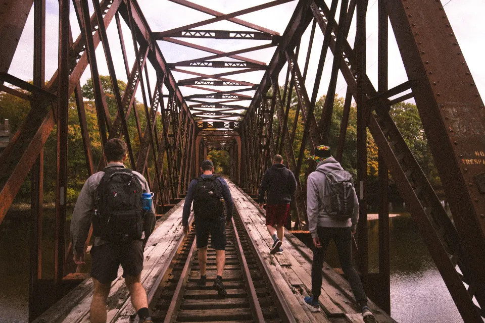 Grupo de amigos caminhando juntos sobre os trilhos de uma ponte de ferro