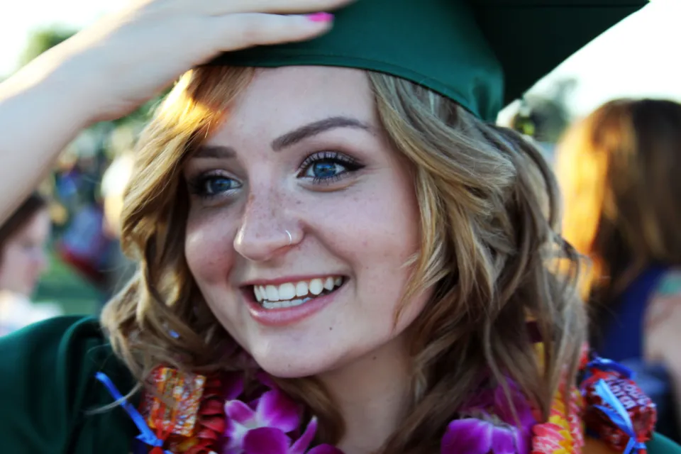 Jovem sorrindo com beca e capelo verdes no dia da formatura