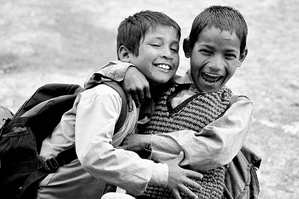Dois meninos com mochilas escolares abraçados e rindo