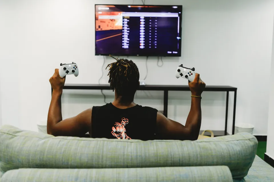 Jovem sentado no sofá jogando videogame diante de uma televisão