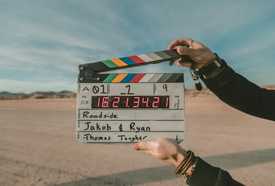 Mãos segurando uma claquete de cinema diante de uma paisagem aberta