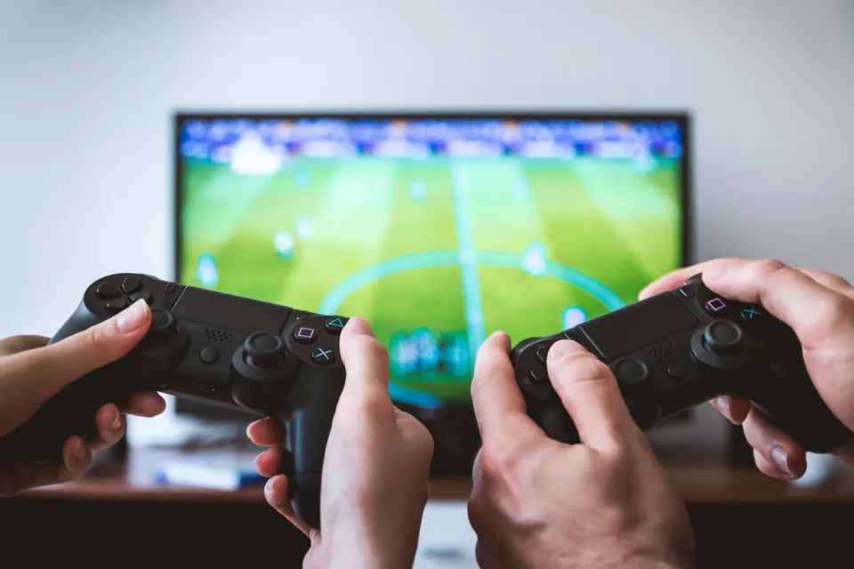 Duas pessoas segurando controles de videogame diante de uma TV com uma partida de futebol
