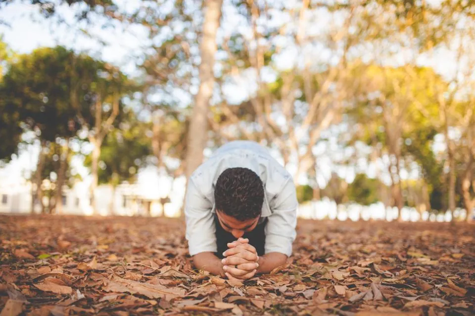 Jovem ajoelhado orando ao ar livre sobre folhas secas