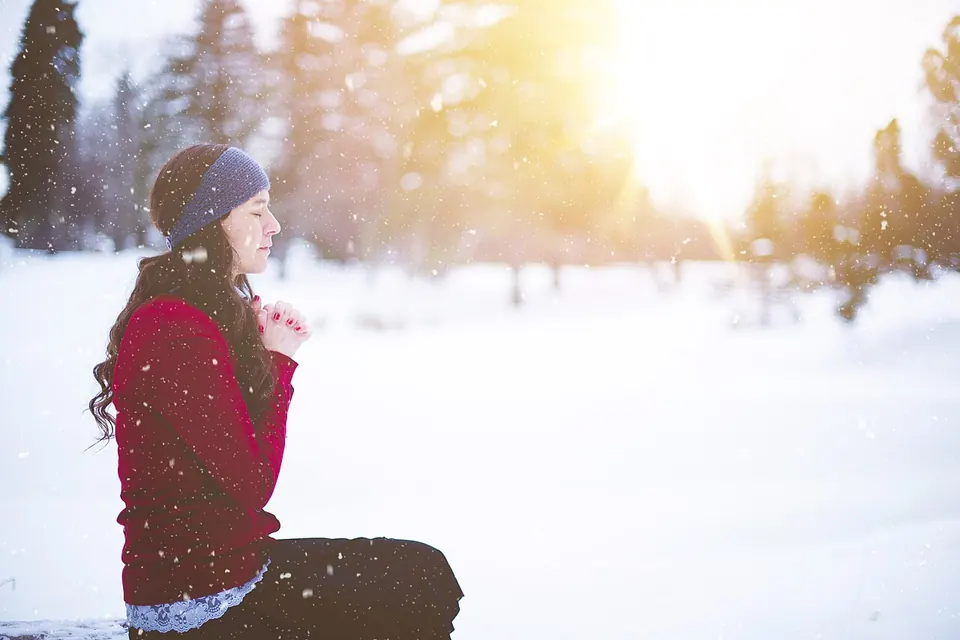 Jovem ajoelhada na neve, de mãos juntas, orando sob a luz do sol