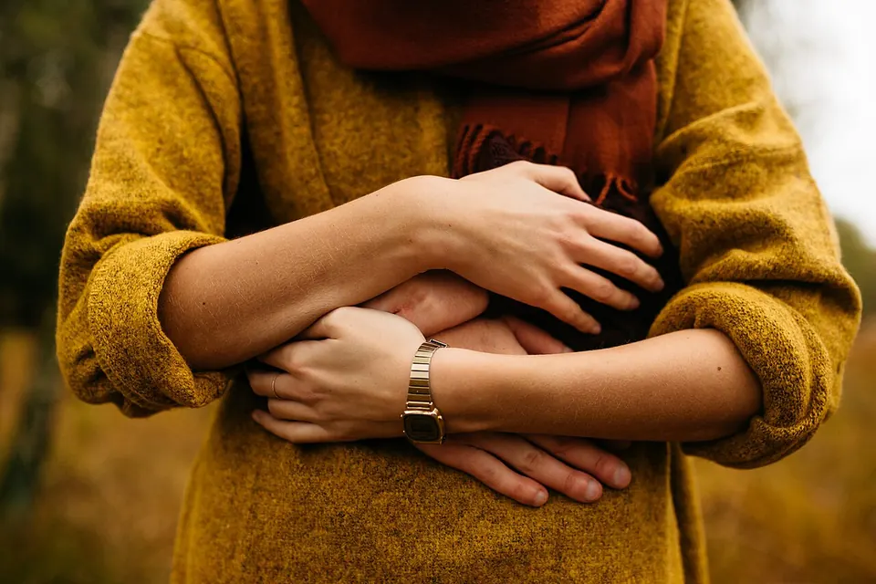Close de mãos se abraçando sobre um suéter amarelo