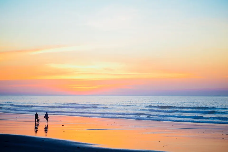 Duas pessoas caminhando na beira da praia ao pôr do sol