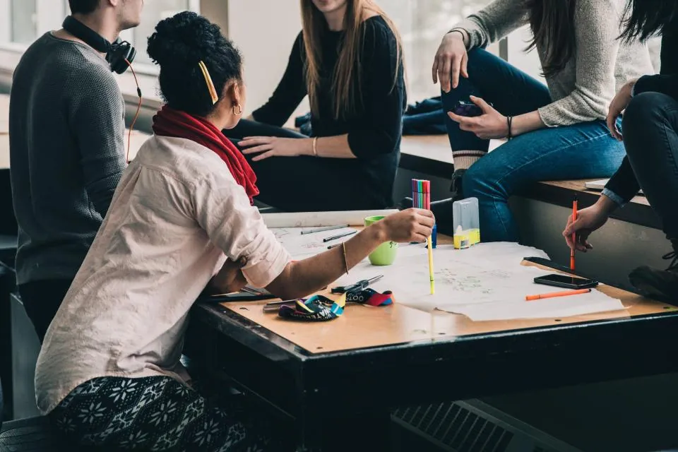 Grupo de estudantes reunidos ao redor de uma mesa, estudando e conversando