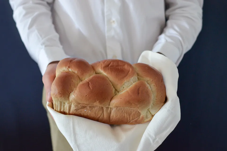 Mãos segurando e oferecendo um pão trançado envolto num pano branco