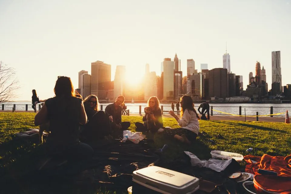 Grupo de amigos sentados juntos na grama observando o pôr do sol sobre a cidade