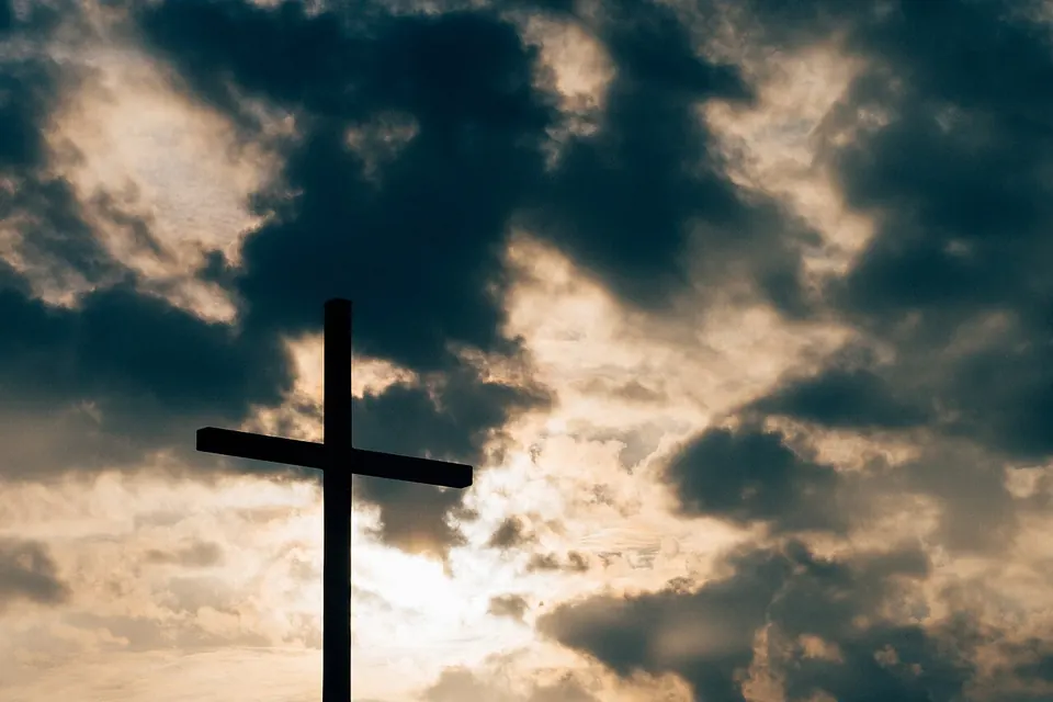 Silhueta de uma cruz contra um céu de nuvens escuras atravessado pela luz do sol