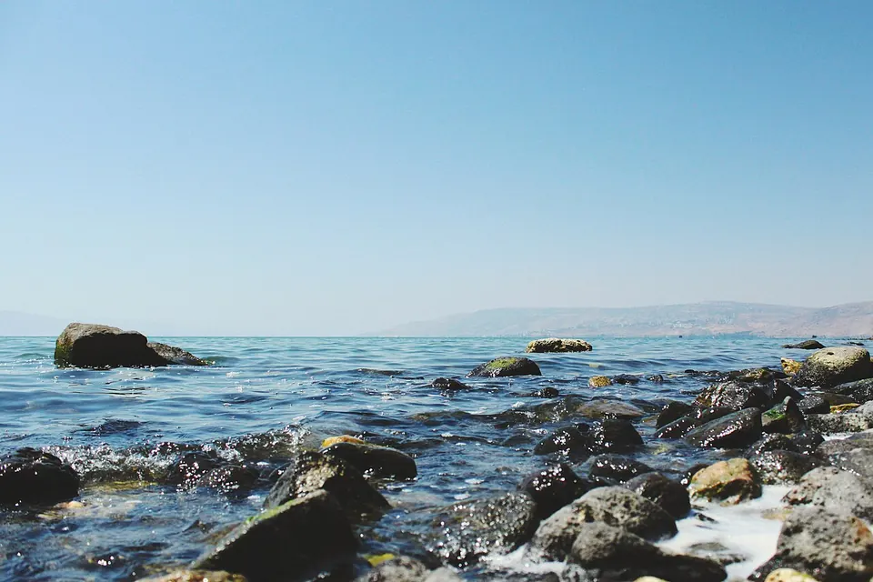 Margem rochosa do mar da Galileia com águas azuis e montanhas ao fundo