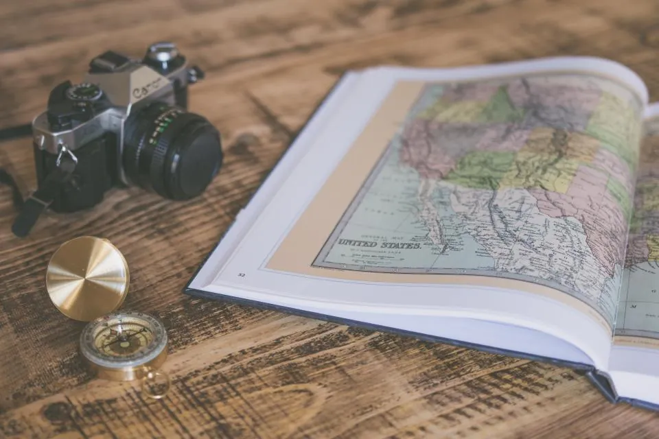 Atlas aberto sobre uma mesa de madeira, com uma bússola e uma câmera antiga
