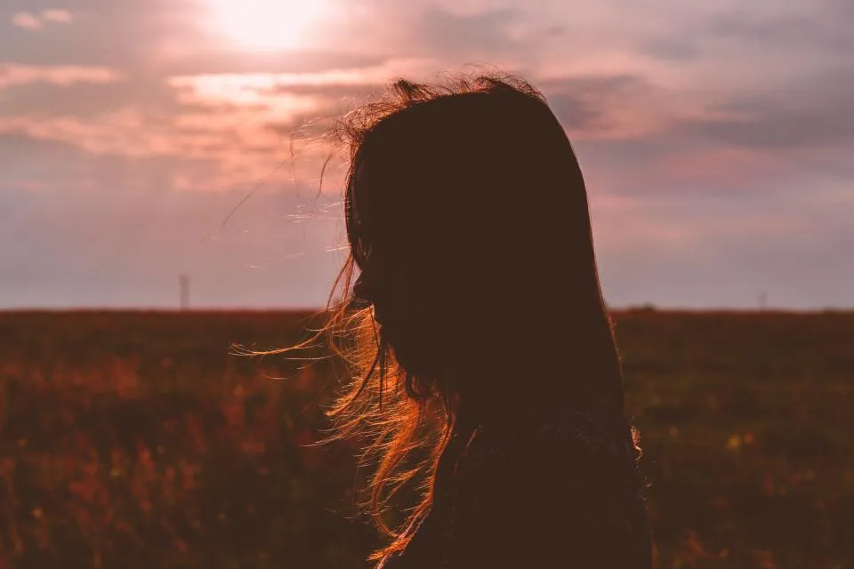 Jovem de costas, com os cabelos ao vento, num campo ao entardecer